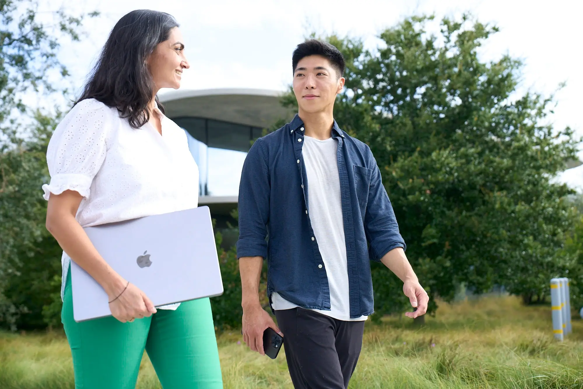 Calvin Iwata walking outdoors with a colleague, both mid-conversation, with Apple Park behind them